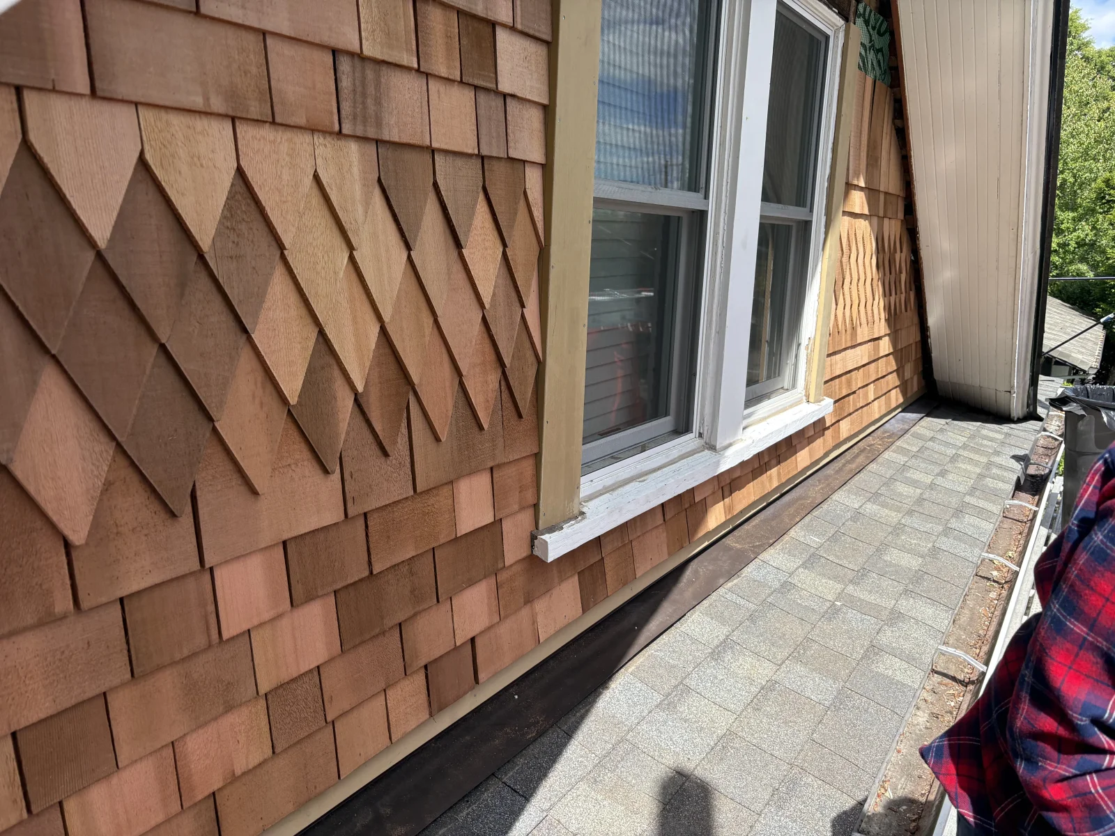 Cedar shake siding with decorative diamond pattern around white double-hung dormer windows and gray asphalt shingle roof
