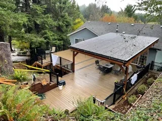Covered composite deck with dark shingle roof, exposed wood posts, and black metal railing